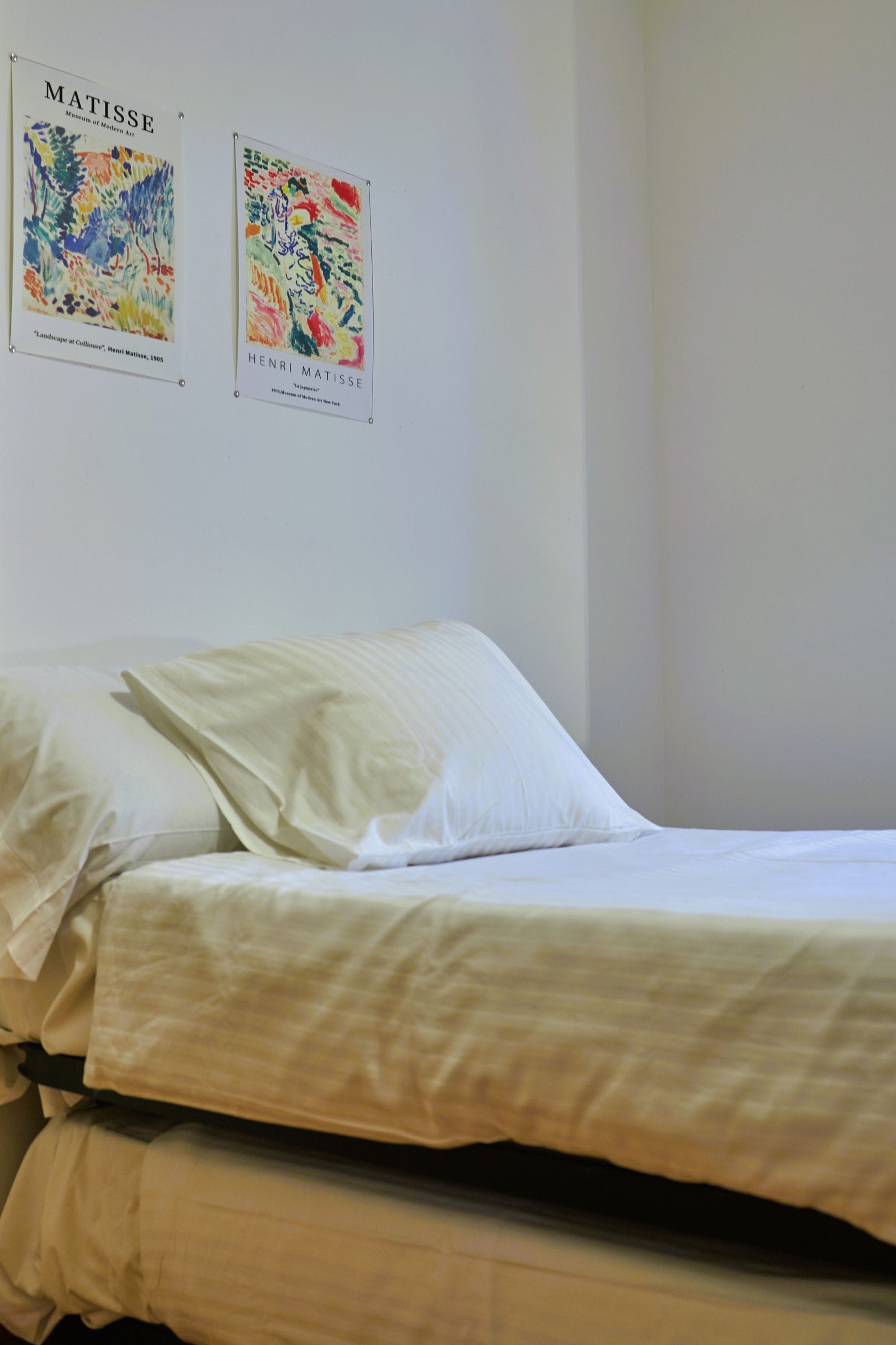 A bed with white linens in a room with two posters on the wall.