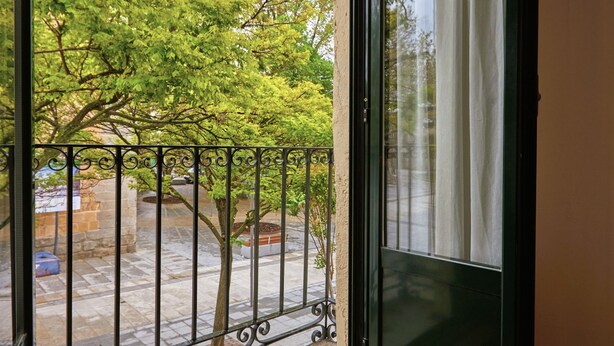 Un balcone con ringhiera in metallo, pavimento in legno e vista su alberi e un edificio sullo sfondo.