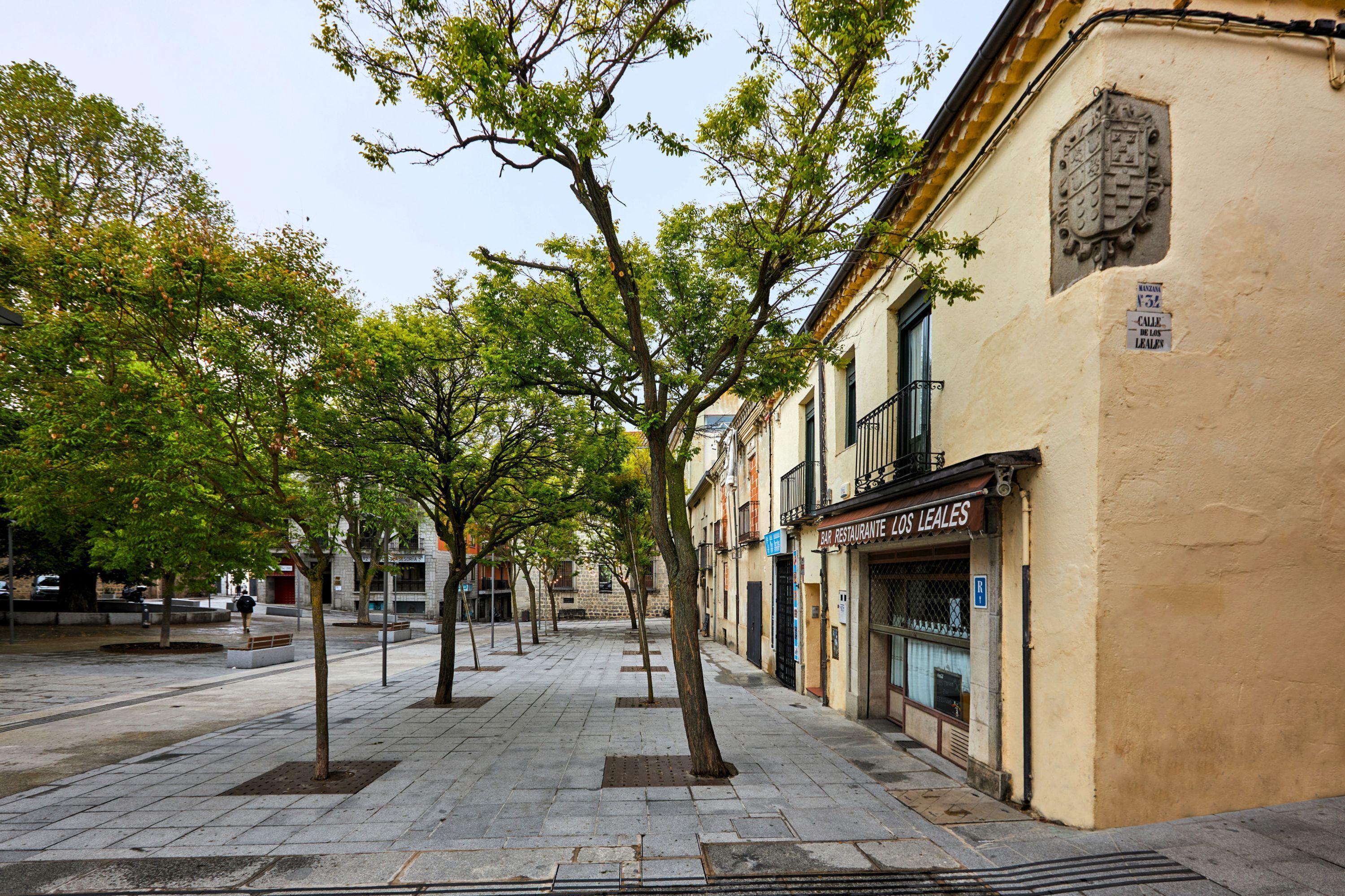 A tree-lined street with a restaurant named "Restaurante Los Leales" on the right.