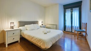 Una camera da letto con un letto, comodini, una sedia, un termosifone e una finestra con tende.