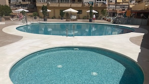 A large, circular pool with a tiled edge, surrounded by a paved area with potted plants and umbrellas. - Tina de Steram Flats Torremolinos (Torremolinos)