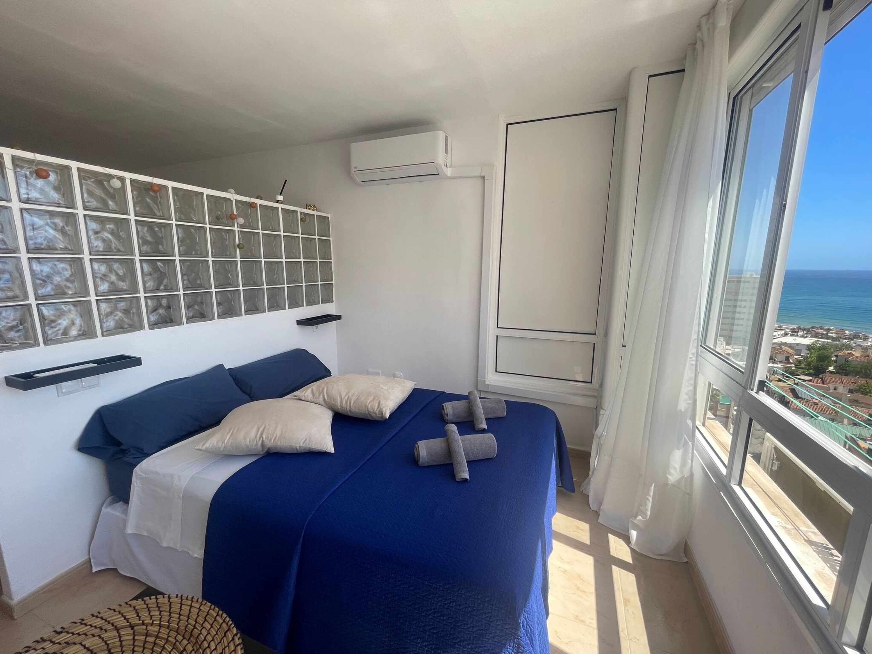 Quarto com cama, janela com vista para o mar e ar condicionado fixado na parede.