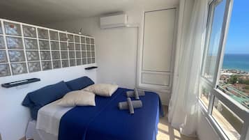 Quarto com cama, janela com vista para o mar e ar condicionado fixado na parede.