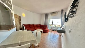 A dining area with a table and chairs, a red sofa, and a small table with a plant.