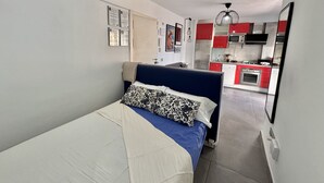 Un dormitorio con cama, mesita de noche y vista a una cocina con armarios rojos y microondas.