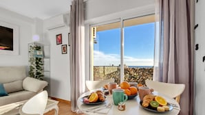 Una sala de estar moderna con comedor, ventanas amplias con vistas a la ciudad, un sofá y una mesa servida con desayuno.