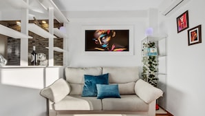 Una sala de estar moderna con un sofá blanco, dos cojines, una obra de arte enmarcada en la pared y un aparador de vidrio con plantas.