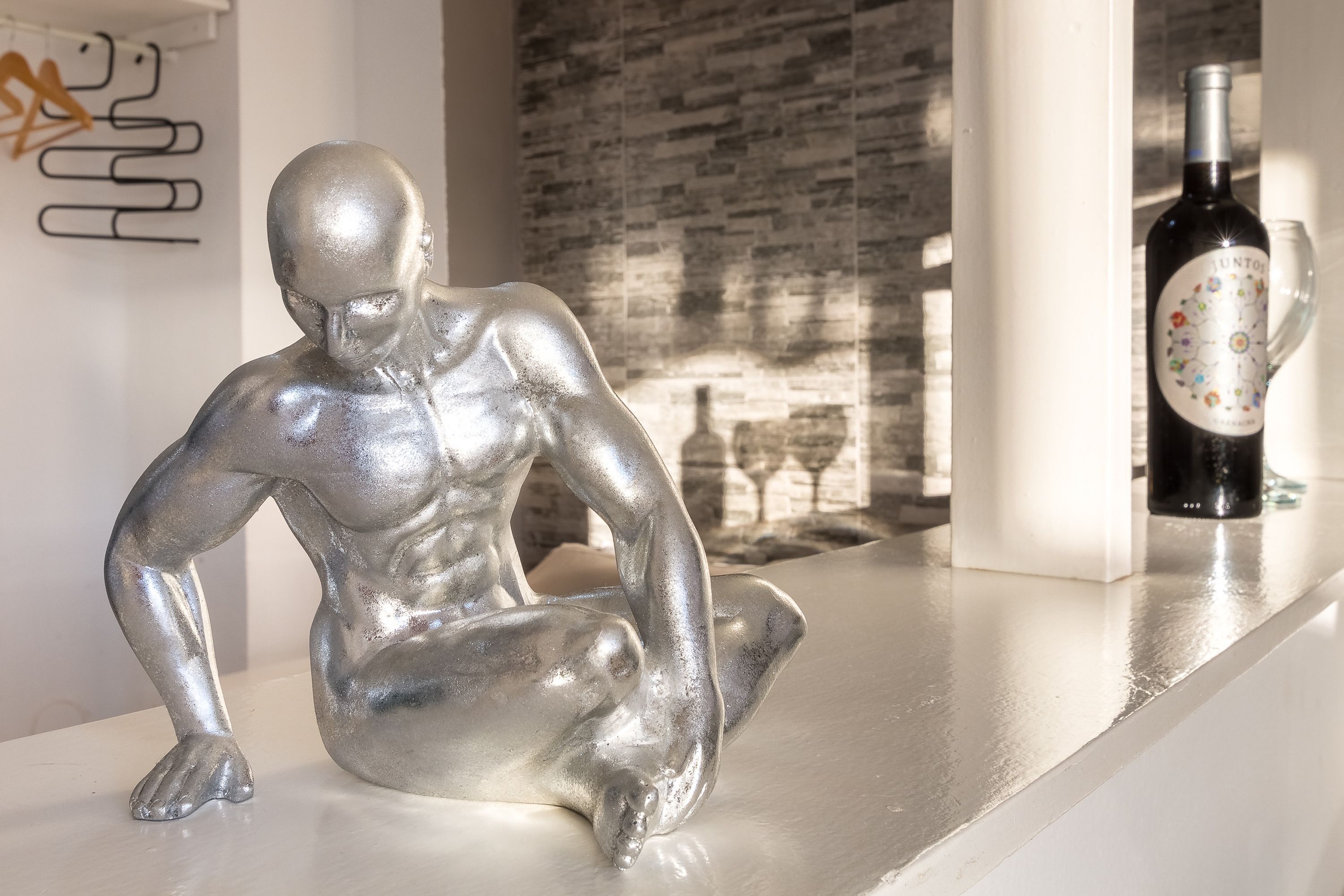 A silver statue on a white countertop, a bottle of wine, and a wine glass.