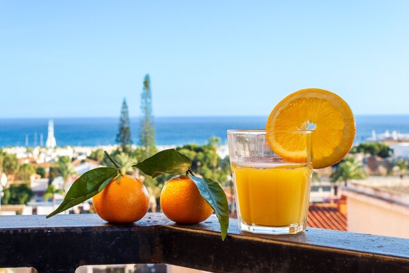A glass of orange juice with a slice of orange on a balcony overlooking a coastal cityscape. - Solpor de Steram Flats Benalmadena (Benalmádena)