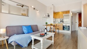A modern living room with a grey sofa, a coffee table with a wine bottle and glasses, a small side table with a lamp, and a kitchen area in the background. - Solpor de Steram Flats Benalmadena (Benalmádena)