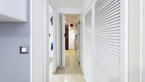 A narrow hallway with a door on the left, a red circular object on the wall, and a white shuttered window on the right. - Noasti de Steram Flats Torremolinos (Torremolinos)