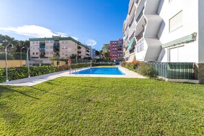 A swimming pool surrounded by well-maintained grass, with multi-story buildings in the background. - Noasti de Steram Flats Torremolinos (Torremolinos)