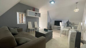 A modern living room with a grey couch, white chairs, a glass coffee table, and a flat-screen TV on a stand. - Noasti de Steram Flats Torremolinos (Torremolinos)