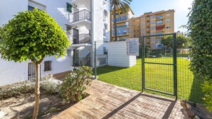 A courtyard with a wooden deck, a fenced area with a palm tree, and a multi-story building with balconies. - Noasti de Steram Flats Torremolinos (Torremolinos)