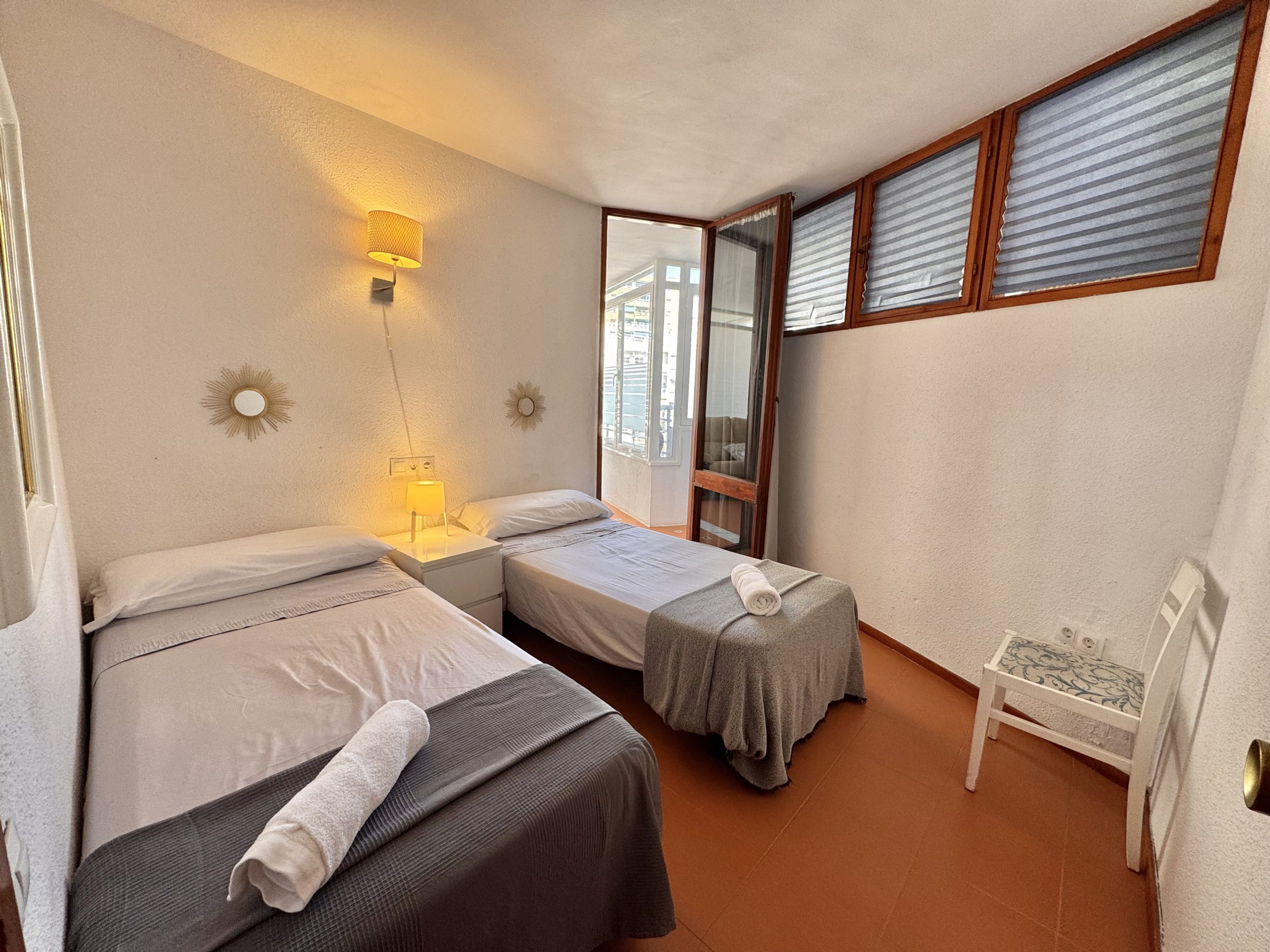 Ein Zimmer mit zwei Betten, einem kleinen Tisch und einem Fenster mit Jalousien.