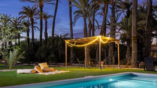 A swimming pool with a pergola and string lights, surrounded by palm trees. - Historical Palms Villa by Fidalsa (Elche)