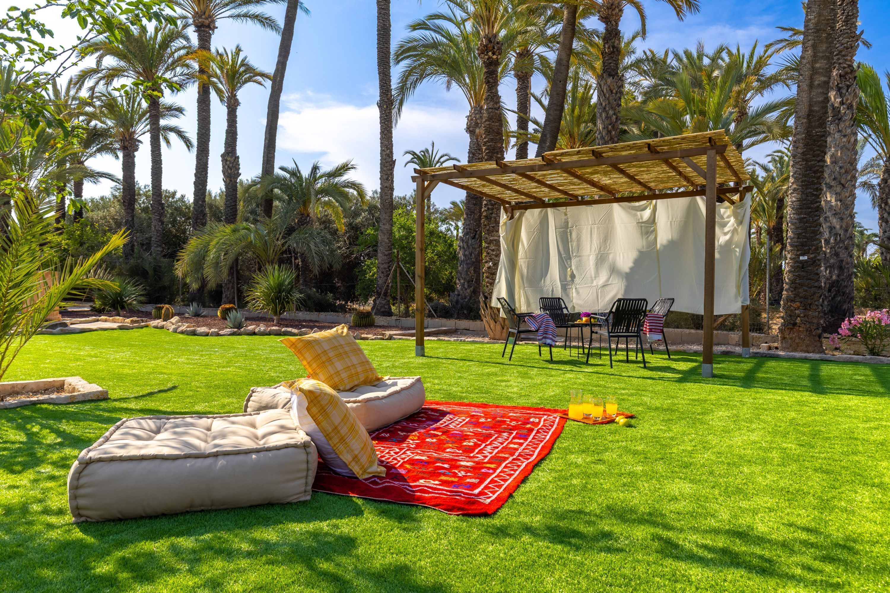A patio area with a covered seating area, a red patterned rug, and a table with drinks.