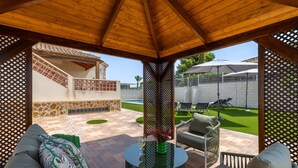 A covered outdoor seating area with a round table, cushioned chairs, and a view of a swimming pool and garden. - Mountain Beautiful by Fidalsa (Busot)
