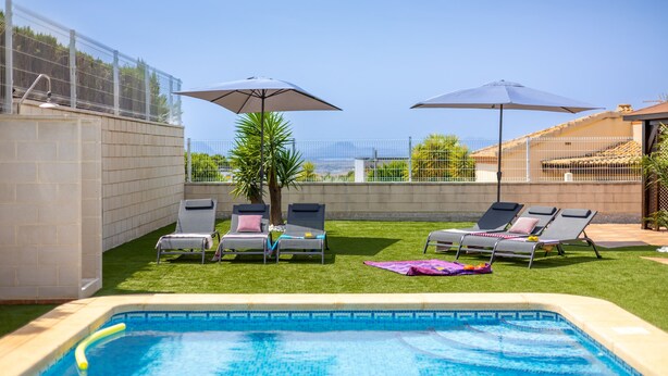 A swimming pool with lounge chairs and umbrellas, surrounded by a fenced yard and a view of the cityscape. - Mountain Beautiful by Fidalsa (Busot)