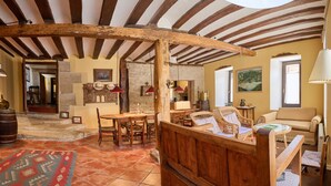A rustic interior with exposed wooden beams, a stone fireplace, a dining area with wooden furniture, and a cozy seating area with a sofa and wicker chairs. - Wine Escape by Fidalsa (Villabuena de Alava)