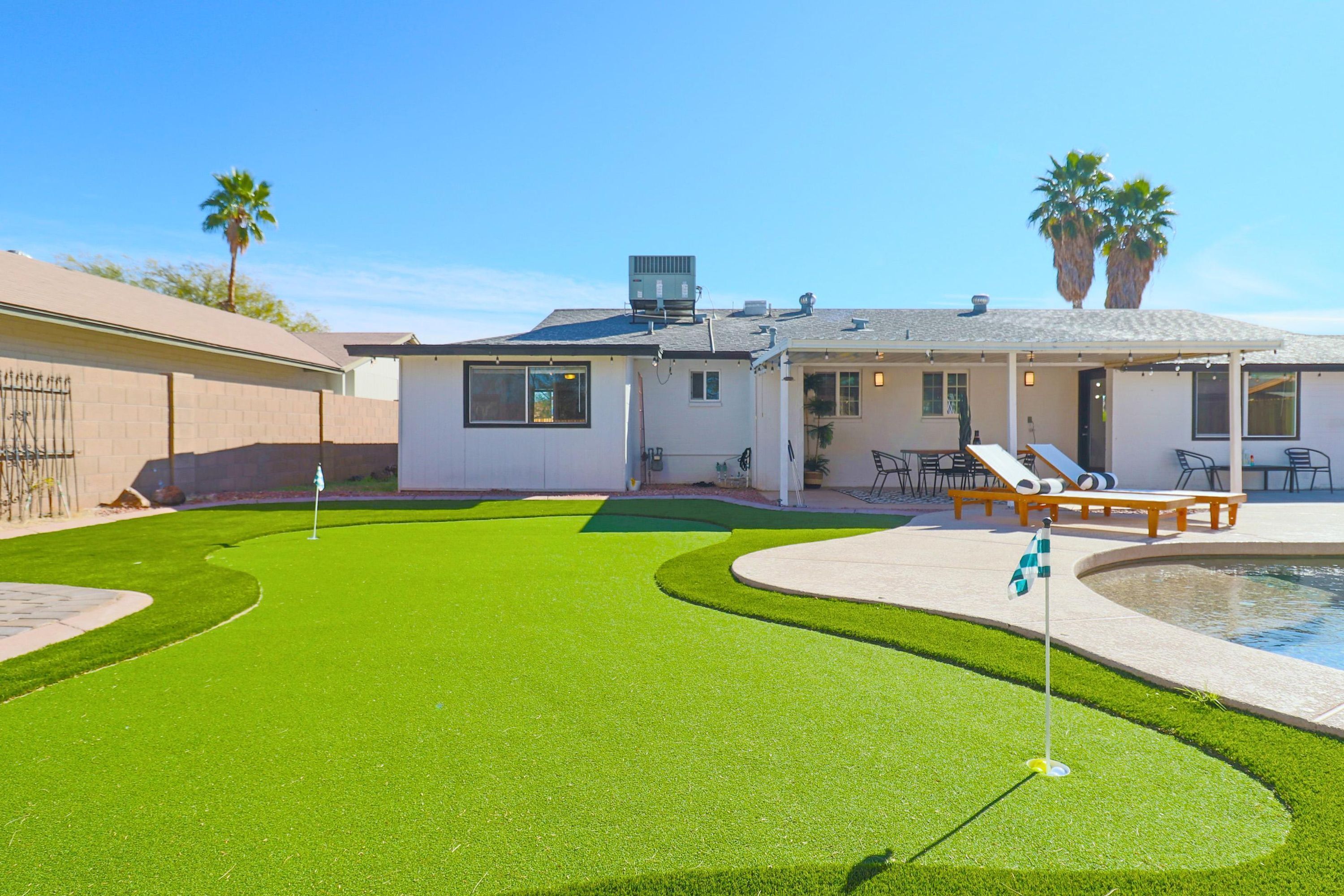 A backyard with a pool, a patio with lounge chairs, and a well-maintained lawn.