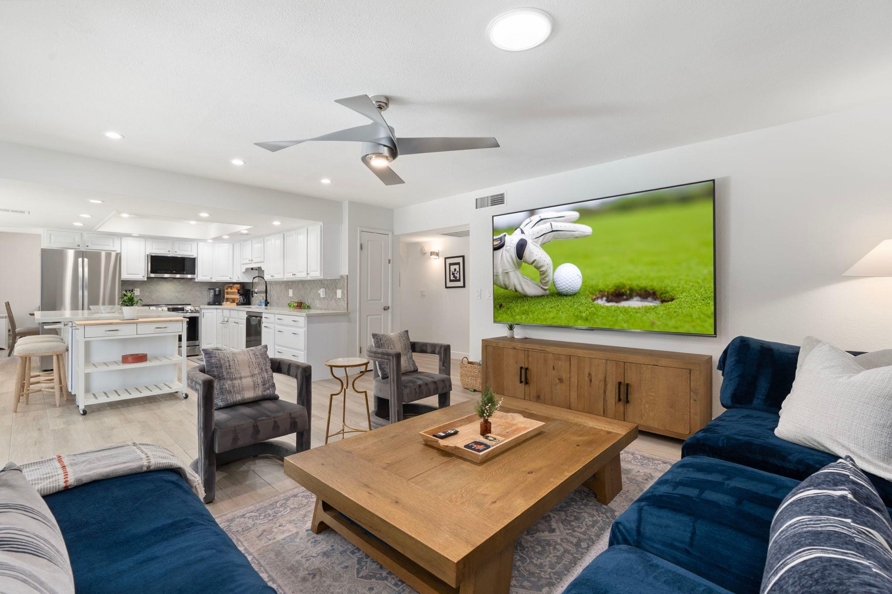 A modern living room with a wooden coffee table, blue sofas, and a TV displaying a golf scene.