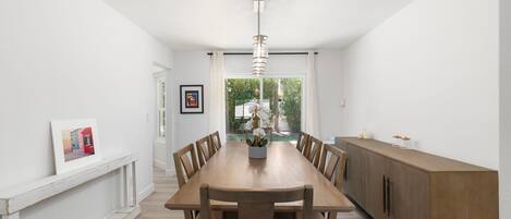 Un comedor con una larga mesa de madera, sillas, un jarrón central con flores y una lámpara colgante.