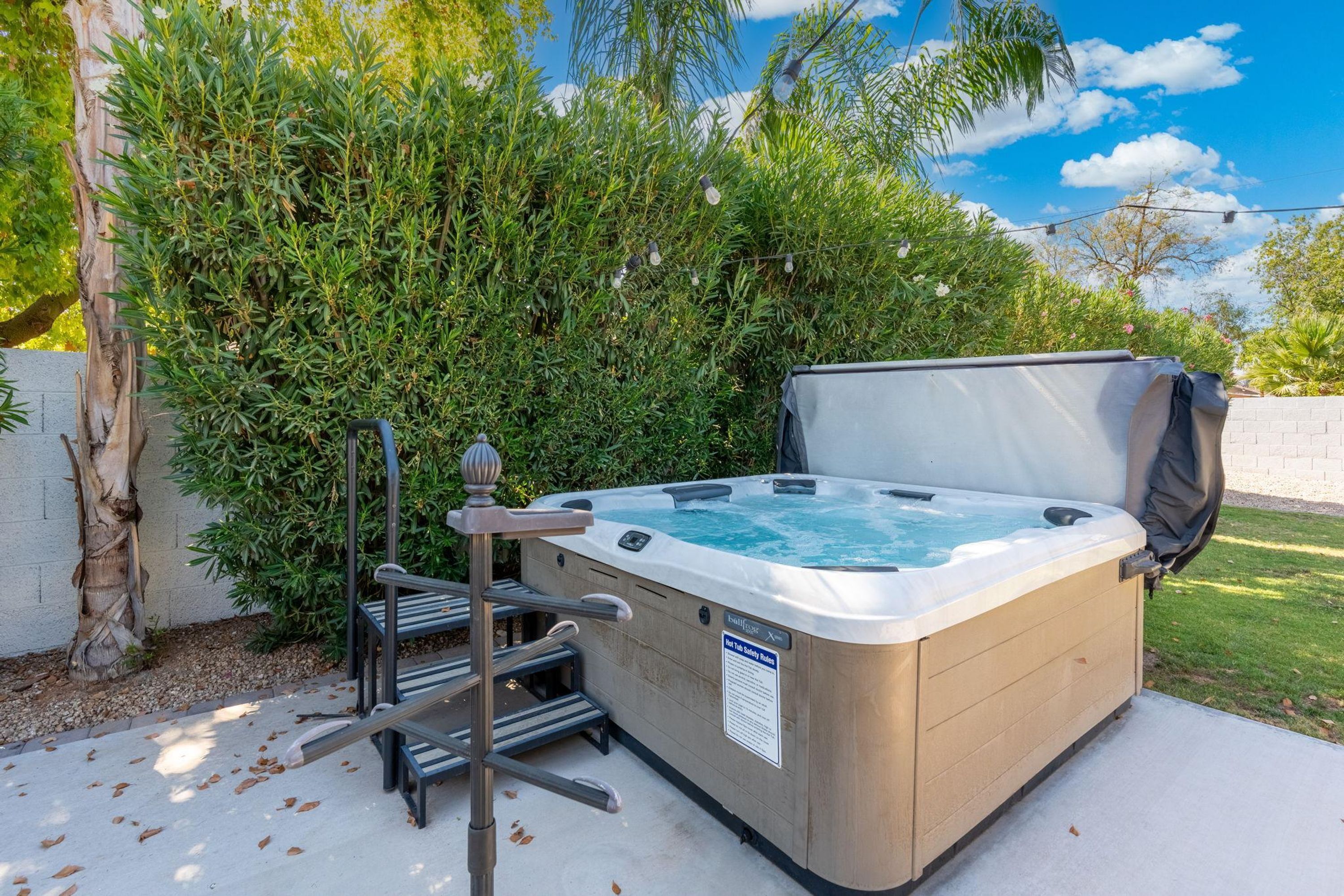 A hot tub with a ladder and steps, surrounded by greenery and a clear sky.