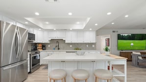 A modern kitchen with white cabinetry, stainless steel appliances, and a large island with stools. - 54th Place in Scottsdale (Scottsdale)