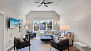 A spacious living room with a high ceiling, a ceiling fan, a large window with a view of the neighborhood, and a flat-screen TV mounted on the wall. - Long Sands Your All-season Getaway (York)