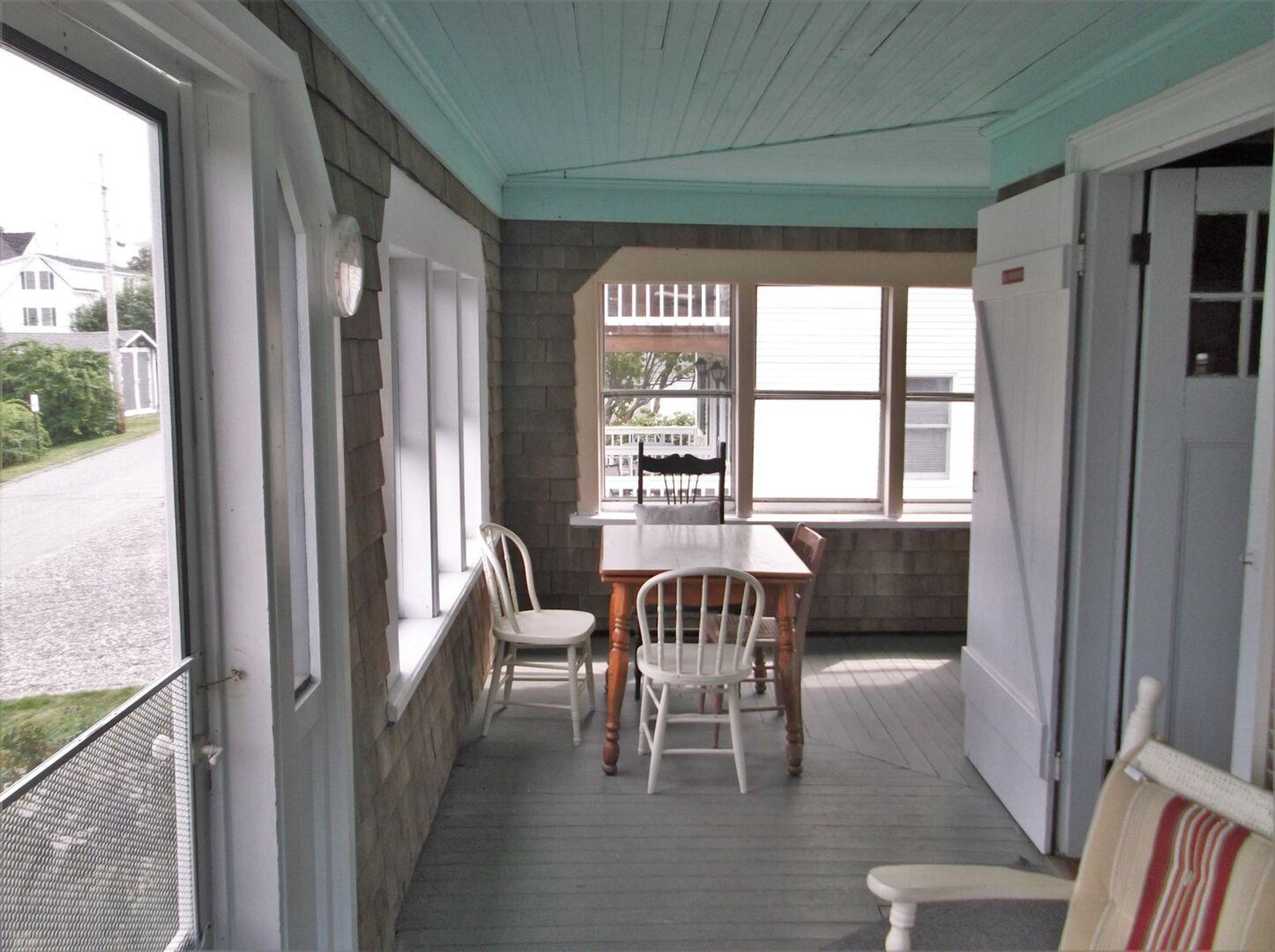 A covered porch with a table and chairs, a view of the street, and a door to the right.