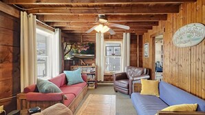 Interior acogedor de una cabaña con paredes de madera, ventilador de techo, un sofá rojo, un sofá azul y una mesa de centro de madera.