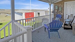 Un porche techado con dos sillas Adirondack, un cobertizo rojo y vista a un campo cubierto de hierba.