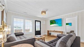 A modern living room with two grey sofas, a wooden coffee table, and a TV on the wall. - Magnolia House in North Myrtle Beach (North Myrtle Beach)