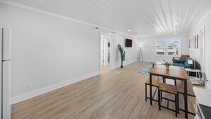 A spacious living area with a wooden floor, white walls, and a dining table with benches. - Surf Sun Pura Vida - 3 (North Myrtle Beach)