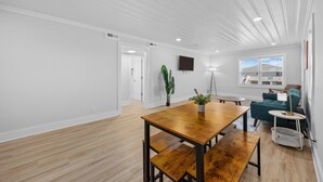 A spacious living area with a wooden dining table, benches, a sofa, and a TV mounted on the wall. - Surf Sun Pura Vida - 3 (North Myrtle Beach)