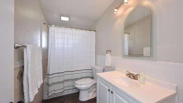 A bathroom with a shower curtain, toilet, sink, and mirror.