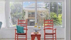 Une pièce avec deux fauteuils à bascule placés face à une fenêtre munie de stores, une petite table sur laquelle est posé un modèle de bateau, et un plaid turquoise sur l’un des fauteuils.