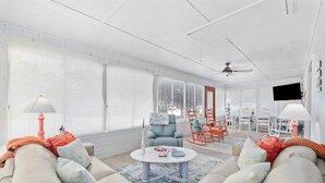Un salon spacieux doté d’une grande fenêtre, d’un ventilateur de plafond et d’un téléviseur fixé au mur.