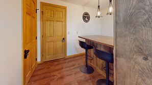 A kitchen with wooden flooring, a wooden door, a bar counter with two stools, and pendant lights. - Beechwood Home in Mendon (Rutland)