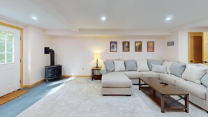 A living room with a sectional sofa, a wooden coffee table, a black fireplace, and a lamp. - Beechwood Home in Mendon (Rutland)