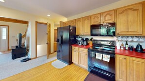 A kitchen with wooden cabinets, a black refrigerator, a stove, and a microwave. - Beechwood Home in Mendon (Rutland)