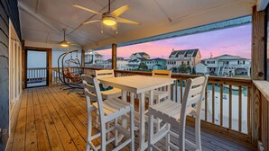 A wooden deck with a table and chairs, a ceiling fan, and a view of houses and a body of water during sunset. - Summer Breeze in North Myrtle Beach (North Myrtle Beach)