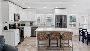 A modern kitchen with white cabinetry, stainless steel appliances, and a central island with bar stools. - Summer Breeze in North Myrtle Beach (North Myrtle Beach)