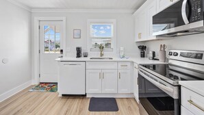 A modern kitchen with white cabinetry, stainless steel appliances, and a large window.