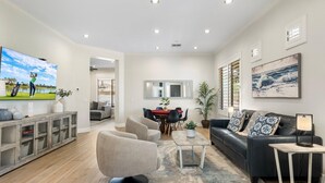 A modern living room with a large flat-screen TV, a black leather sofa, a dining area with a red table, and a large mirror on the wall. - Dublin in Gilbert With 4 Bedrooms and 2 Bathrooms (Gilbert)