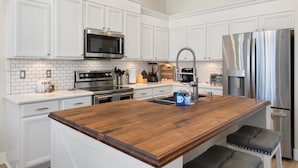 A modern kitchen with white cabinetry, stainless steel appliances, a wooden island, and bar stools. - Dublin in Gilbert With 4 Bedrooms and 2 Bathrooms (Gilbert)