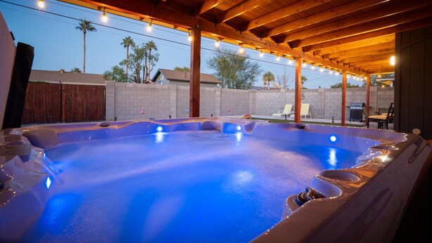 A hot tub under a wooden pergola with string lights, surrounded by a brick wall and palm trees. - Devonshire in Scottsdale (Scottsdale)