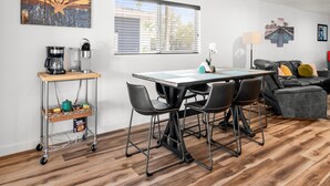 A modern living room with a dining area, featuring a coffee station, a sofa, and a window with blinds. - Devonshire in Scottsdale (Scottsdale)