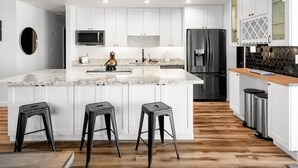 A modern kitchen with white cabinets, a granite countertop, stainless steel appliances, and three black stools. - Devonshire in Scottsdale (Scottsdale)